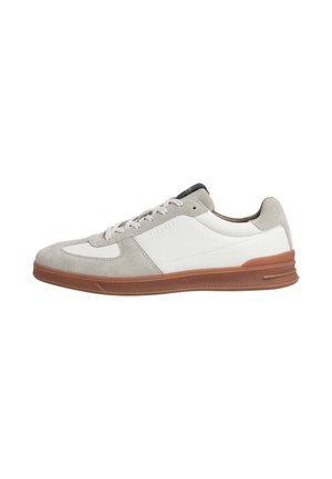 Lage sneaker met beige suède en witte leren bovenzijde, bruine rubberen zool en witte veters, gezien van de buitenkant.