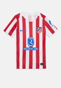 Crveno-bijela prugasta nogometna majica s V-izrezom, koja sadrži logo Atletico Madrida, plavi sponzor "Riyadh Air" i Nikeov amblem.