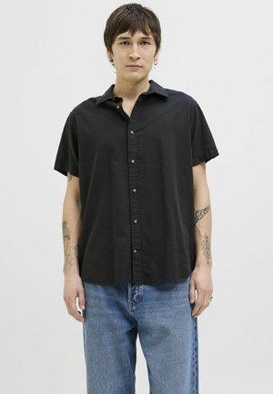 Black short-sleeve button-up shirt with a collared design, smooth texture, and contrasting buttons, paired with blue denim pants.