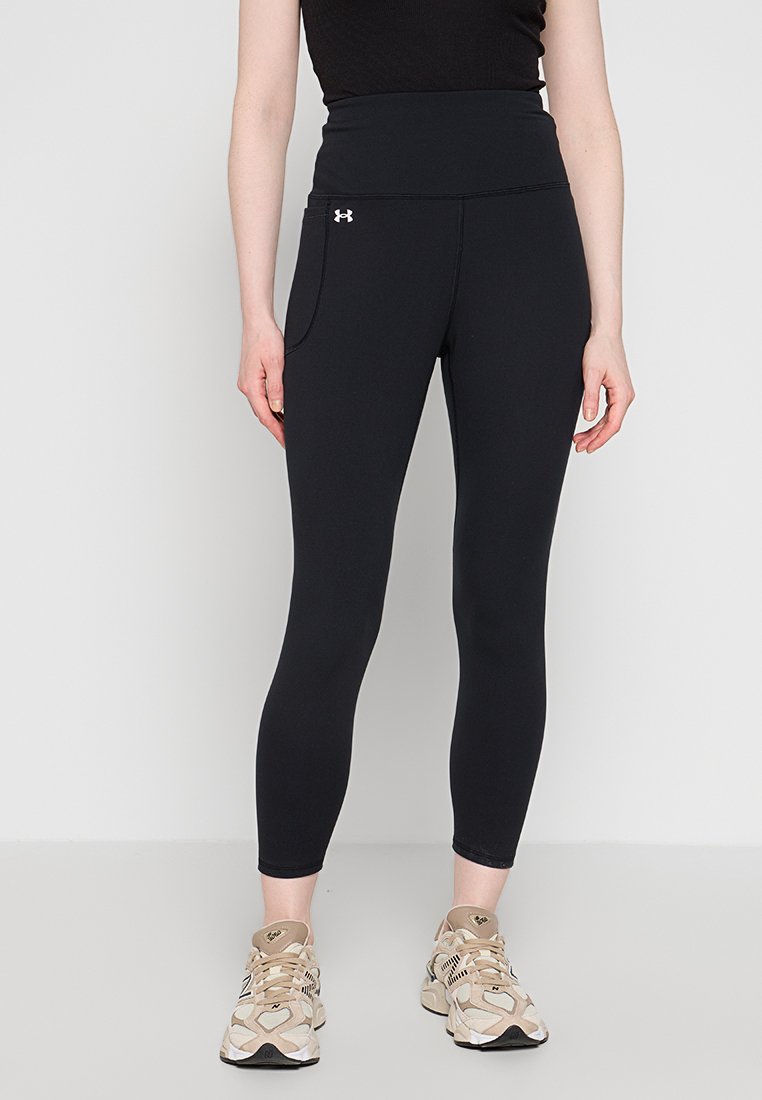 Leggings neri a vita alta realizzati in materiale elasticizzato, con una tasca laterale e una superficie liscia. Indossati con scarpe da atletica beige.