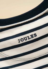 Gros plan sur un tissu à rayures bleu marine et blanches avec un col côtelé bleu marine et le mot « JOULES » brodé en fil bleu marine.