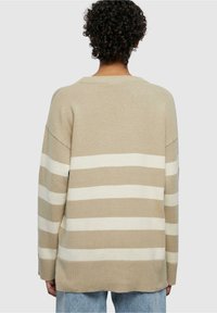 Pull en beige et blanc à rayures, coupe relaxée, col rond et épaules tombantes. Tissu tricoté doux, détail d'ourlet arrière plus long.