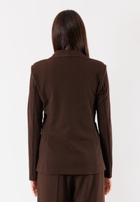 Blazer marrone su misura con colletto a sciallata, maniche lunghe e silhouette aderente, mostrato da dietro su uno sfondo bianco.