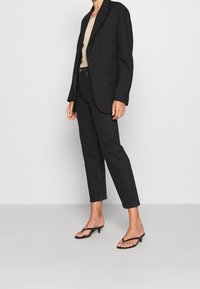 Svart oversized kavaj över en beige topp, matchad med högmidjade svarta jeans och svarta klacksandaler. Enkel design, skräddarsydd passform.