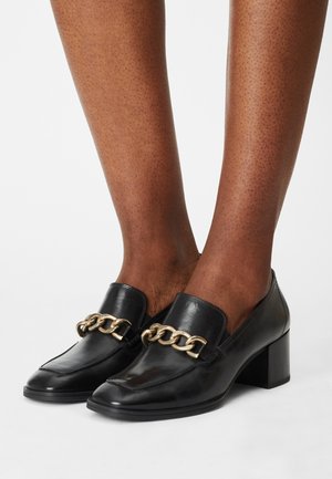 Czarne skórzane mokasyny na słupku, z złotym łańcuchem zdobiącym przód. Gładka faktura i szpiczasty kształt noska.