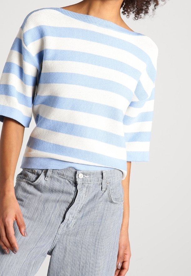 Pull en maille rayé bleu clair et blanc avec un large décolleté et des manches courtes, associé à un jean gris clair rayé.