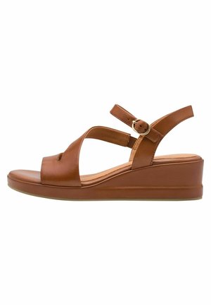 Sandales compensées en cuir marron avec design à lanières croisées, bride de cheville ajustable et semelle intérieure rembourrée pour le confort. Texture lisse, détails minimalistes.