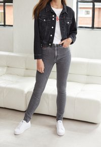 Chaqueta vaquera en azul oscuro, camiseta blanca con logo rojo, vaqueros ajustados grises y zapatillas blancas. Textura suave y diseño entallado.