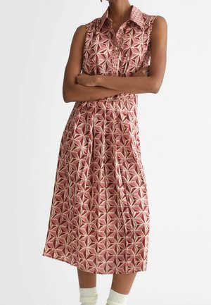 Sukienka midi bez rękawów z kołnierzykiem, w różowo-beżowy geometryczny wzór gwiazdek, z przodu na guziki, plisowana spódnica, noszona z białymi skarpetkami.