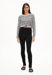 Zwarte leggings gecombineerd met een cropped zwart-wit gestreepte langefsleevetop. Model draagt donkere slippers. Eenvoudig en aansluitend ontwerp.