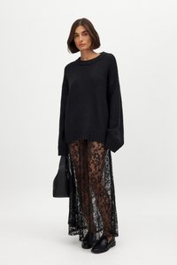 Sort oversized striktrøje med rund halsudskæring, parret med gennemsigtige sorte lacedragtbukser med blomsterprint. Sorte flade sko og taske inkluderet.