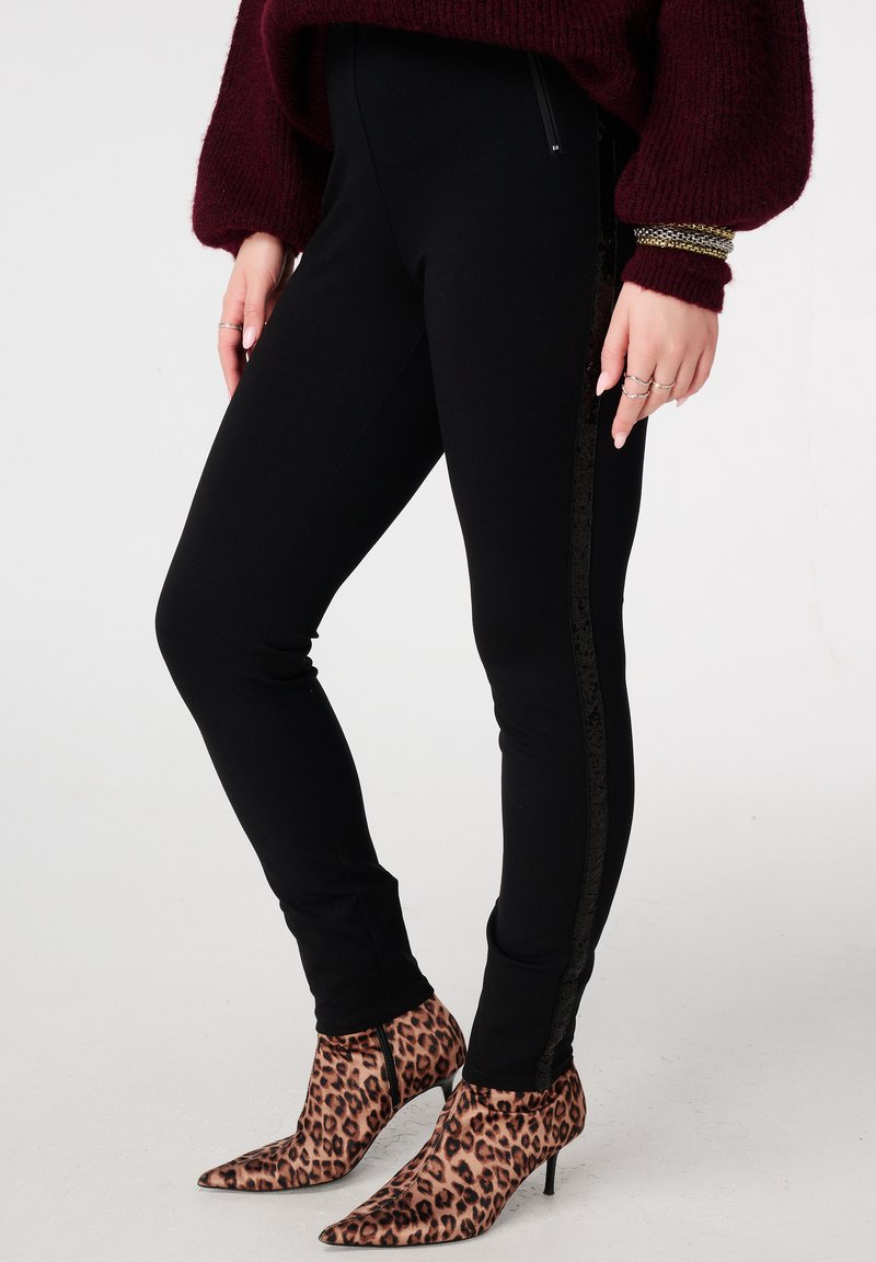 Zwarte legging met een glanzende zwarte zijstreep, gecombineerd met spitse enkellaarsjes met luipaardprint. Gebreide bordeauxrode trui met volumineuze mouwen.