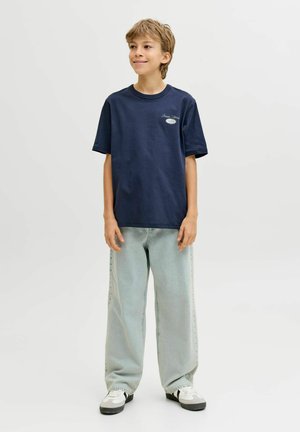 Tumesinist puuvillast t-särk ümara kaelusega ja lühikeste varrukatega; rinnal väike logo. Sobitatud helesiniste laiade säärega teksadega.