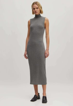 Robe sans manches grise avec un col haut, fabriquée en un matériau tricoté lisse, tombant jusqu'au mollet, accompagnée de chaussures noires à enfiler.