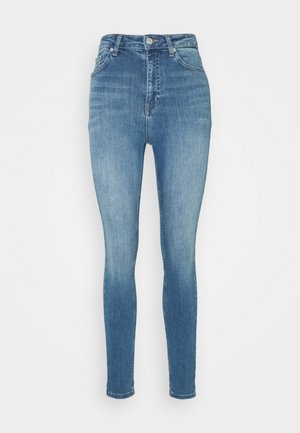 Aukštos stovinės lieknos džinsai mėlynos denim medžiagos. Yra lygus paviršius, išblukusios vietos, penkių kišenių dizainas, metalinis mygtuko uždarymas ir diržo kilpos.