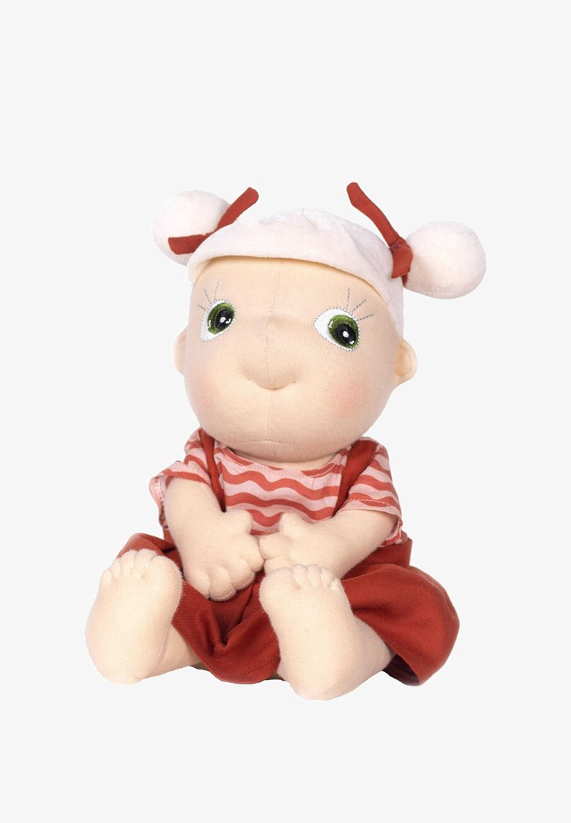 Miękka lalka z materiału, z zielonymi oczami, uśmiechniętą twarzą, paskowanym czerwonym topem, czerwoną spódnicą i białym kapeluszem z pomponami. Charakteryzuje się szczegółowym haftem na twarzy.