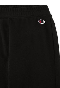 Zwarte joggingbroek van zachte stof met een elastische tailleband en een klein wit en rood logo aan de bovenlinkerkant.