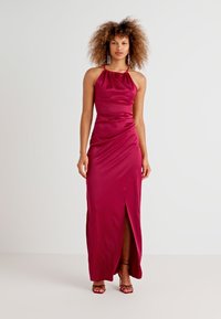 Εφαρμοστό φόρεμα με ψηλό λαιμό σε μπορντό σατέν, που διαθέτει πτυχώσεις στην πλευρά και σκίσιμο ως το thigh. Αποτελείται από κόκκινες strappy γόβες και κρεμαστά σκουλαρίκια.