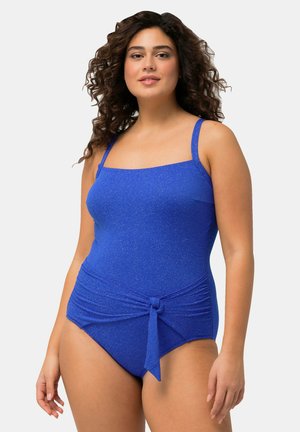 Costume da bagno blu con scollatura dritta, spalline sottili e dettagli annodati in vita. Il tessuto ha un leggero luccichio.
