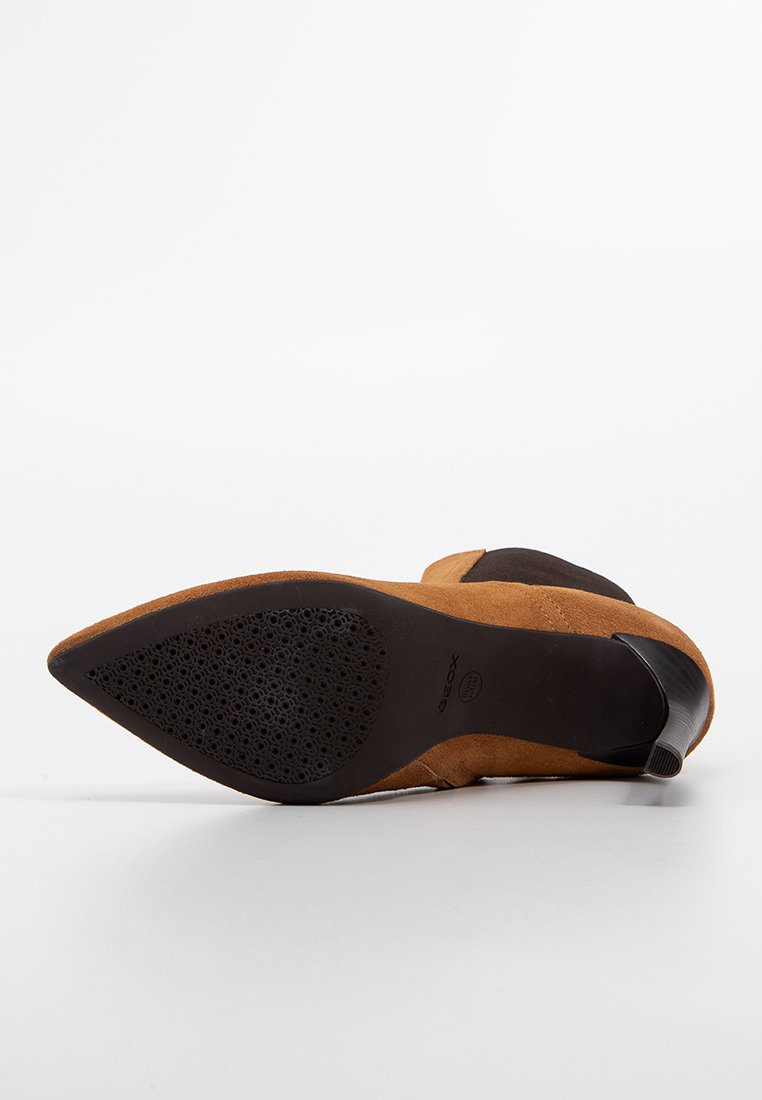 Stivale alla caviglia in suede marrone con punta affusolata, suola nera robusta e dettaglio con taglio laterale. Il tacco è basso e presenta accenti testurizzati.