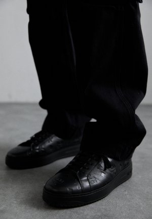 Black leather sneakers with textured patterns, featuring a rubber sole and round toe. Laces are black, complementing the shoe’s dark design.