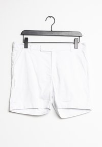 Bermudas de algodón blancas colgadas en una percha negra. Presentan bolsillos frontales y una textura suave y libre de arrugas con un diseño limpio y simple.