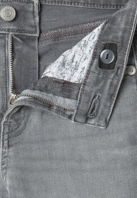 Jeans de denim gris con un cierre metálico, cierre de botón y forro interior con un patrón. La tela tiene una textura suave.