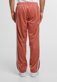 Sportliche Hosen in roséfarbener Nuance, aus glattem Stoff; mit weißen seitlichen Streifen und elastischem Bund für zusätzlichen Komfort. Sauberer, taillierter Schnitt.