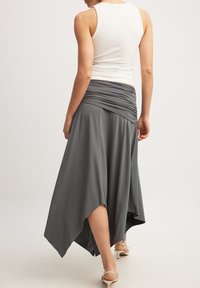 Harmaa, virtaava hame, jossa on kootut vyötärönauha ja epäsymmetrinen helma, yhdistettynä tiukkaan valkoiseen toppiin. Tasainen tekstuuri, elegantti laskos.