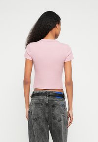 Ροζ ριμπ κορμάκι με κοντά μανίκια, συνδυασμένο με ψηλόμεσο ξεβαμμένο μαύρο τζιν με μπλε λεπτομέρεια στη ζώνη.