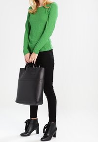 Maglietta verde a maniche lunghe, jeans skinny neri, stivaletti neri con tacco e borsa a tracolla nera strutturata con doppi manici.