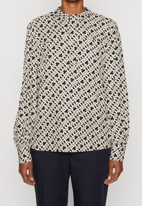 Long-sleeve blouse in black and cream geometric pattern, featuring a rounded neckline and elasticized cuffs, made from lightweight fabric.