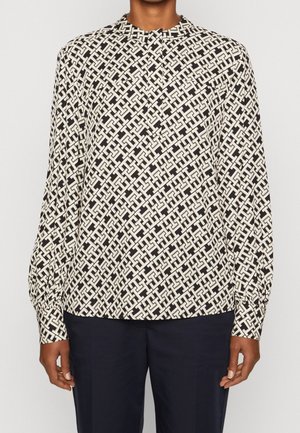 Long-sleeve blouse in black and cream geometric pattern, featuring a rounded neckline and elasticized cuffs, made from lightweight fabric.