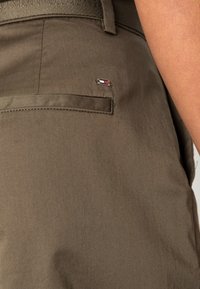 Olivgrön bomullsblandade byxor med en bakficka med sydda detaljer och ett litet emblem med röda, vita och blå accenter.