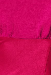 Tissu rose vif avec deux textures distinctes : l'une douce et veloutée, l'autre nervurée et froncée le long d'une couture.