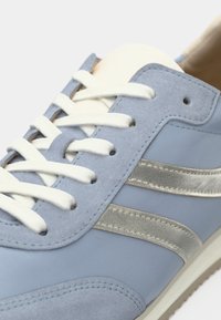 Ανοιχτό μπλε δερμάτινο αθλητικό παπούτσι με λευκά κορδόνια, μεταλλικές ασημί ρίγες στα πλαϊνά και λεία υφή. Διαθέτει επένδυση στη γλώσσα και στο εσωτερικό.