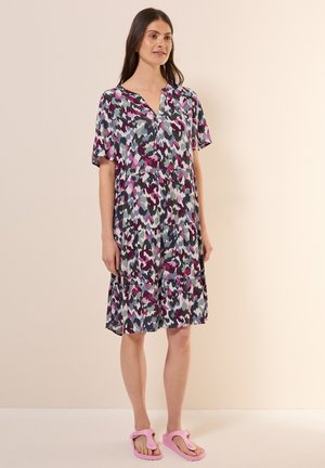 Blommigt mönstrad klänning i nyanser av lila, grå och teal, med korta ärmar, v-ringning och volangdesign. Tillsammans med rosa flip-flops.