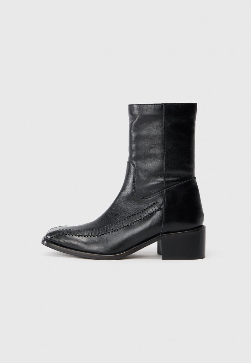 Juodas odinis kulkšninis botas su smailiu pirštu, dekoratyvine siuvinėjimo linija šone ir storu kvadratiniu kulnu. Lygus paviršius, minimalistinis dizainas.