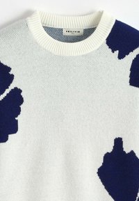 Pull en tricot blanc avec des patches abstraits irréguliers bleu marine et un col ras du cou côtelé, étiqueté taille M par Frilivin.