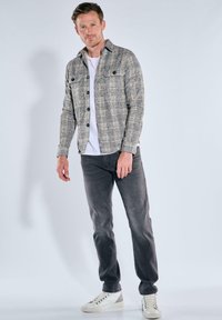 Graues karriertes Hemdjacke mit zwei Brusttaschen, kombiniert mit einem weißen T-Shirt, grauen Jeans und weißen Sneakern. Schlichtes Design und lässige Passform.