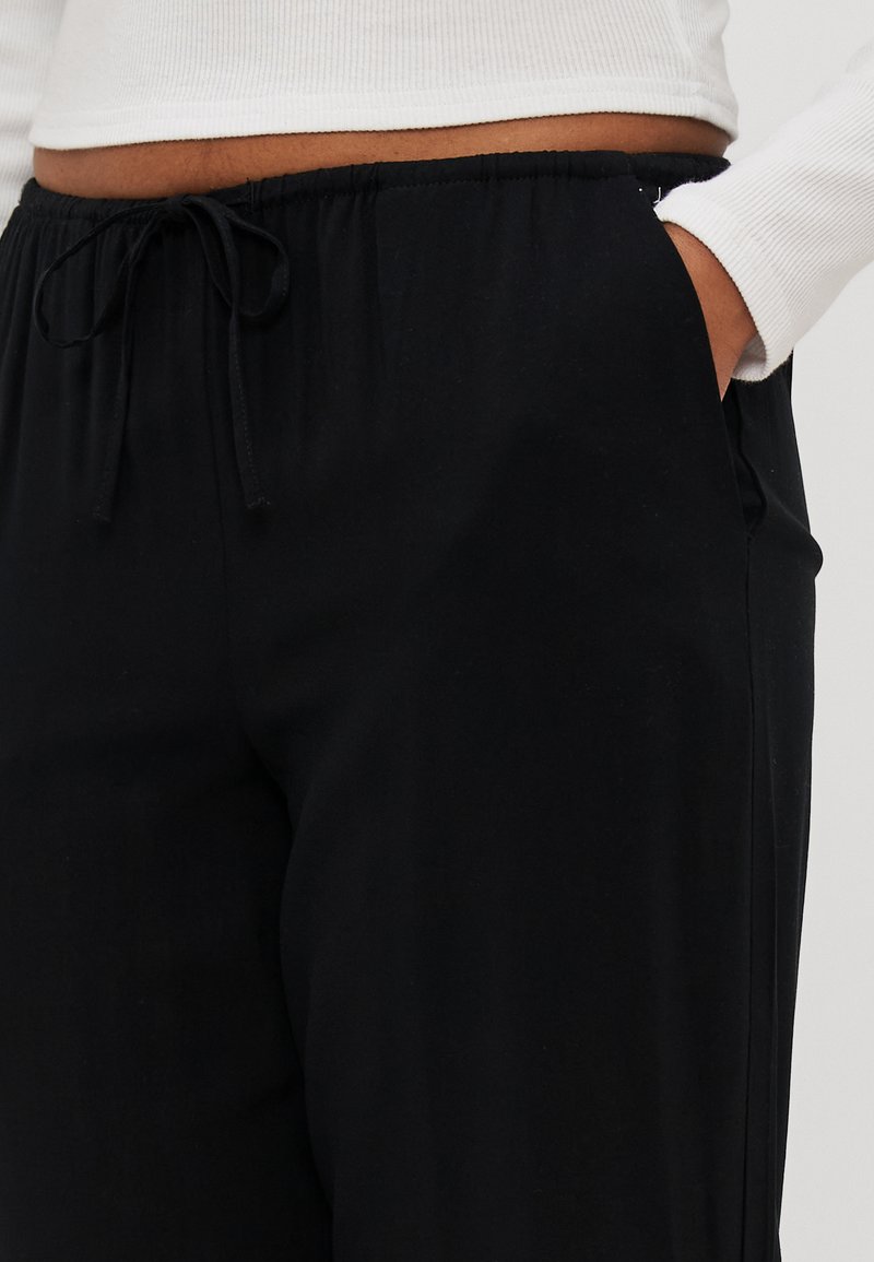 Pantalon noir avec une taille élastique et un cordon de serrage. Le tissu semble doux avec une texture lisse. Il dispose de poches latérales pour plus de fonctionnalité.