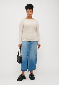 Beige hosszú ujjú felső, kék farmer maxiszoknya elülső hasítékkal, fekete vastag talpú slip-on cipő és egy kis fekete kézitáska.