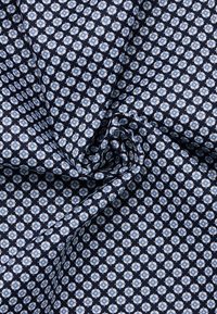 Tessuto di cotone con un motivo geometrico di fiori blu chiaro su uno sfondo blu navy scuro; la texture appare liscia e tessuta.
