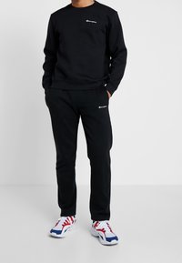 Sudadera negra y pantalones jogger hechos de una suave mezcla de algodón; con acentos de logo en blanco; combinados con zapatillas deportivas coloridas.