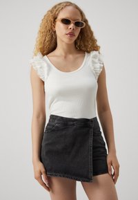 Hvit ribbet tank topp med volanger på ermene, sammen med et svart denim omslagskjørt med knappeåpning og frontlommer.