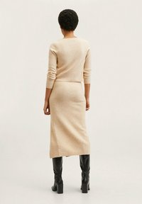 Beżowy zestaw swetra i spódnicy z dzianiny, dopasowany krój, miękka tekstura; połączony z czarnymi wysokimi botkami na obcasie, gładkie wykończenie.