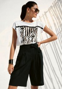 White t-shirt with black and orange zebra stripes, paired with high-waisted black shorts featuring a front tie and pleats.