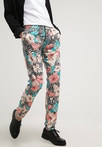 Pantalons à motifs présentant un design floral avec des accents roses et teal, sur un fond à rayures noires et blanches. Ceinture élastique.