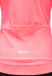 Κοντινό πλάνο φωτεινής ροζ ποδηλατικής φανέλας από πίσω με τρεις υφασμάτινες τσέπες και το λευκό λογότυπο "Rapha." κεντραρισμένο πάνω από το τελείωμα.