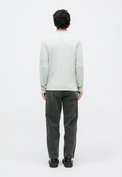 Jasnoszara koszula z długim rękawem o okrągłym dekolcie, z centralnym szwem. Połączona z ciemnoszarymi spodniami luźnymi i czarnymi butami.